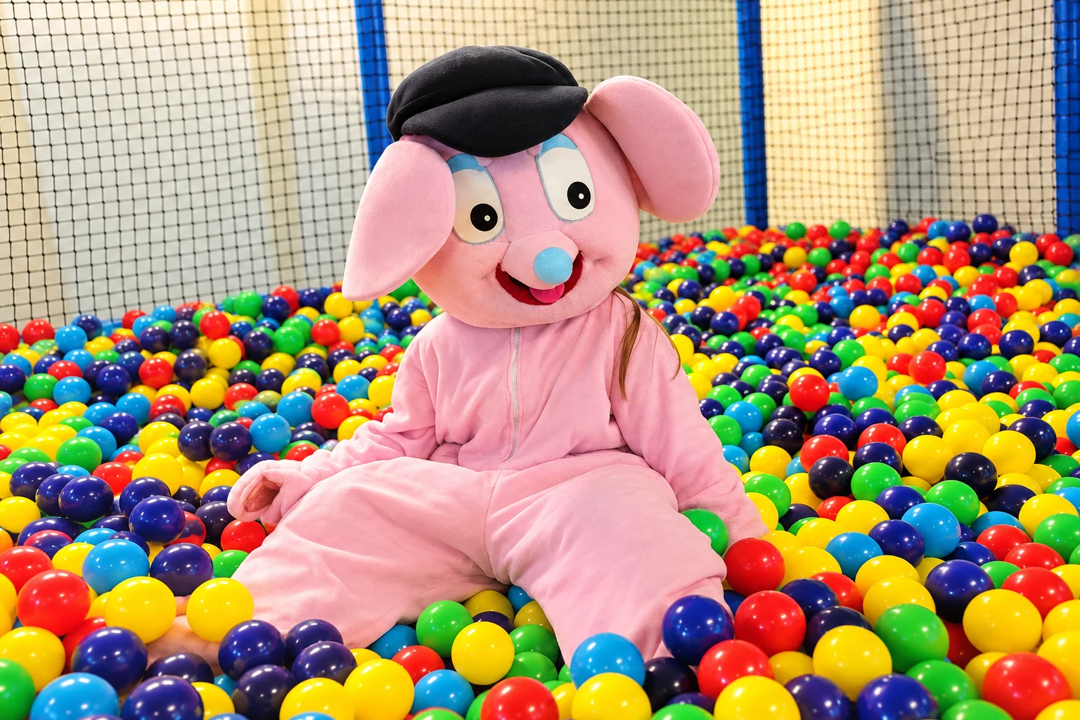 Lekstans rosa elefantmaskot i ett färgglatt bollhav